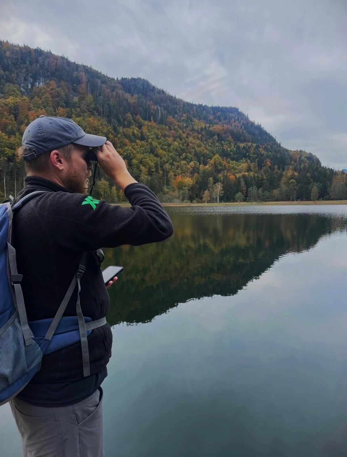 Mark looking through binoculars beside a mountain lake